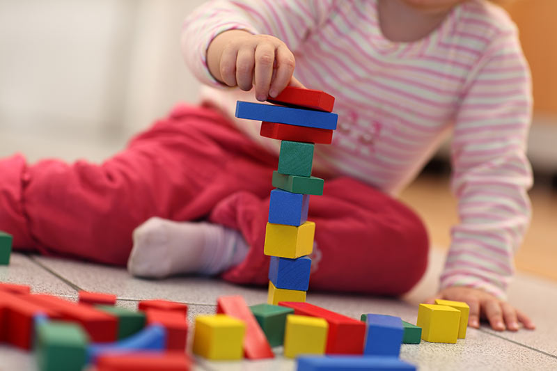 Kind sitzt auf dem Boden und spielt mit Buklötzern