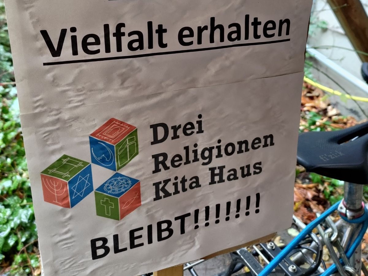 Demostrationsschild: Vielfalt erhalten. Drei-Religionen-Kita-Haus bleibt!